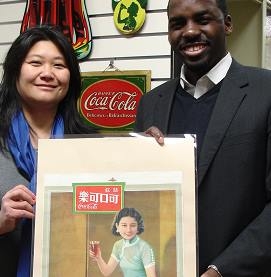 APALA member Tricia Sung (L) and Jamal Booker (R), Coca-Cola Company Archivist, at the Coca-Cola Company Archives, 2013. Both are holding up an advertising poster published in 1936 and used in American Chinatowns.