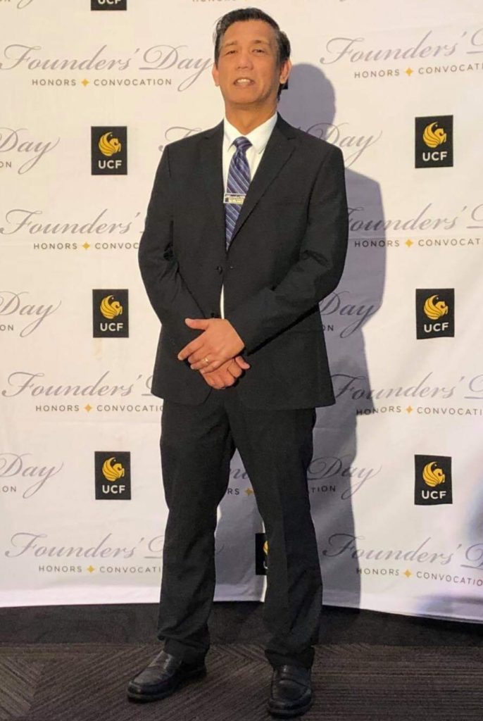 APALA past Executive Director Ven Bosco posing in front of a red-carpet style banner.