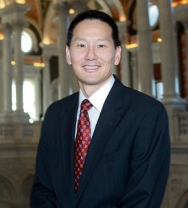 image of David Mao, Deputy Librarian of Congress. An Asian American man in a dark suit wearing a reddish tie with the interior of Library of Congress in the background.