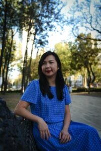 Photo of author Cathy Linh Che in a blue dress on a bench.