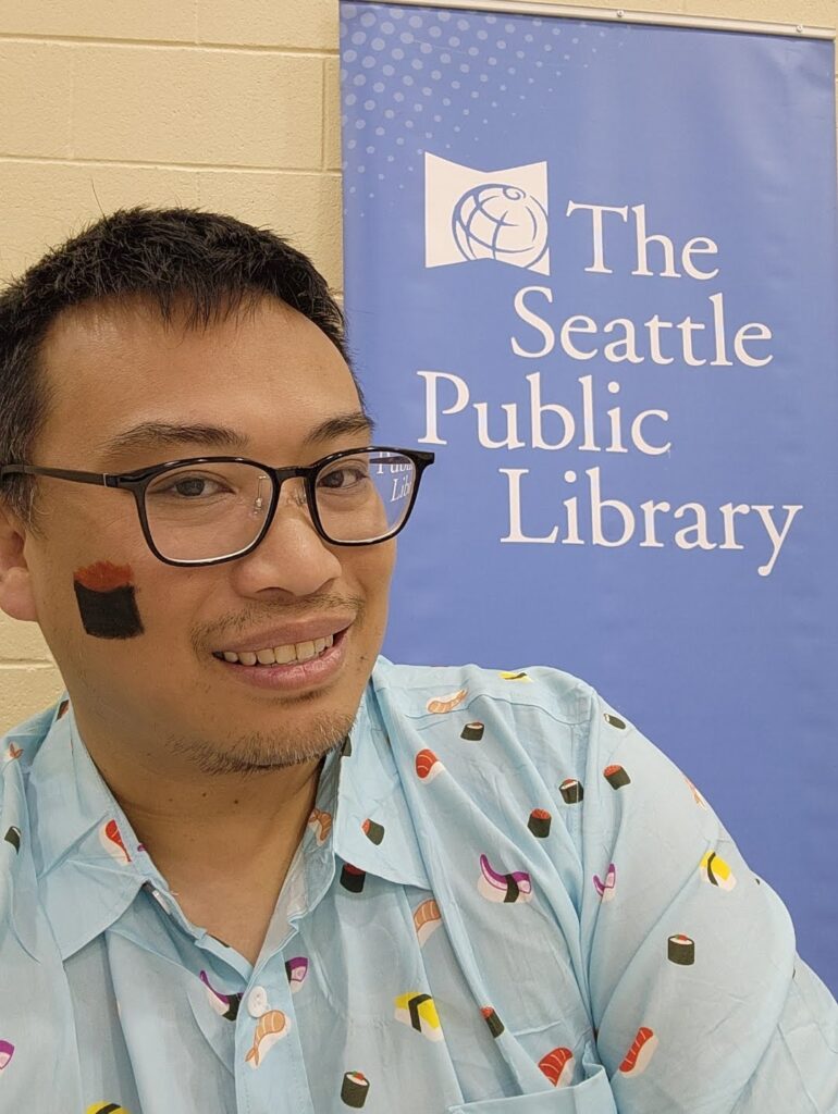 Librarian Warren Chin, with glasses and a light blue collared shirt, beside a blue banner that reads The Seattle Public Library